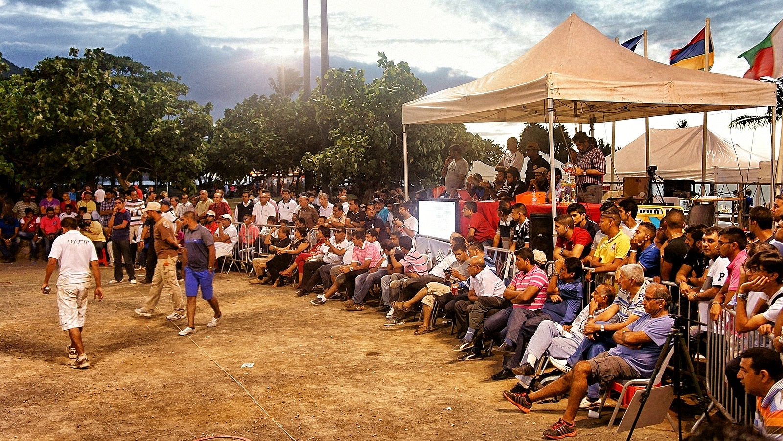 Concours de pétanque en soirée, joueurs et public autour du terrain