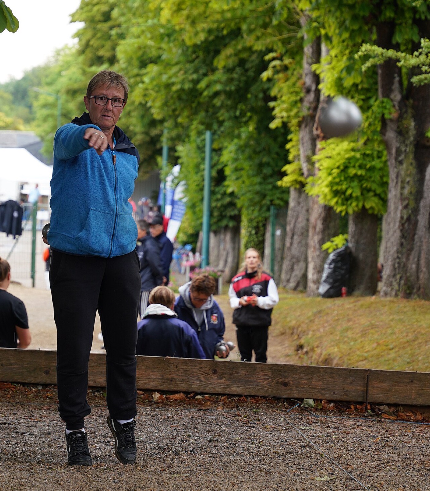 Joueuse en plein lancer de boule sur un terrain de pétanque